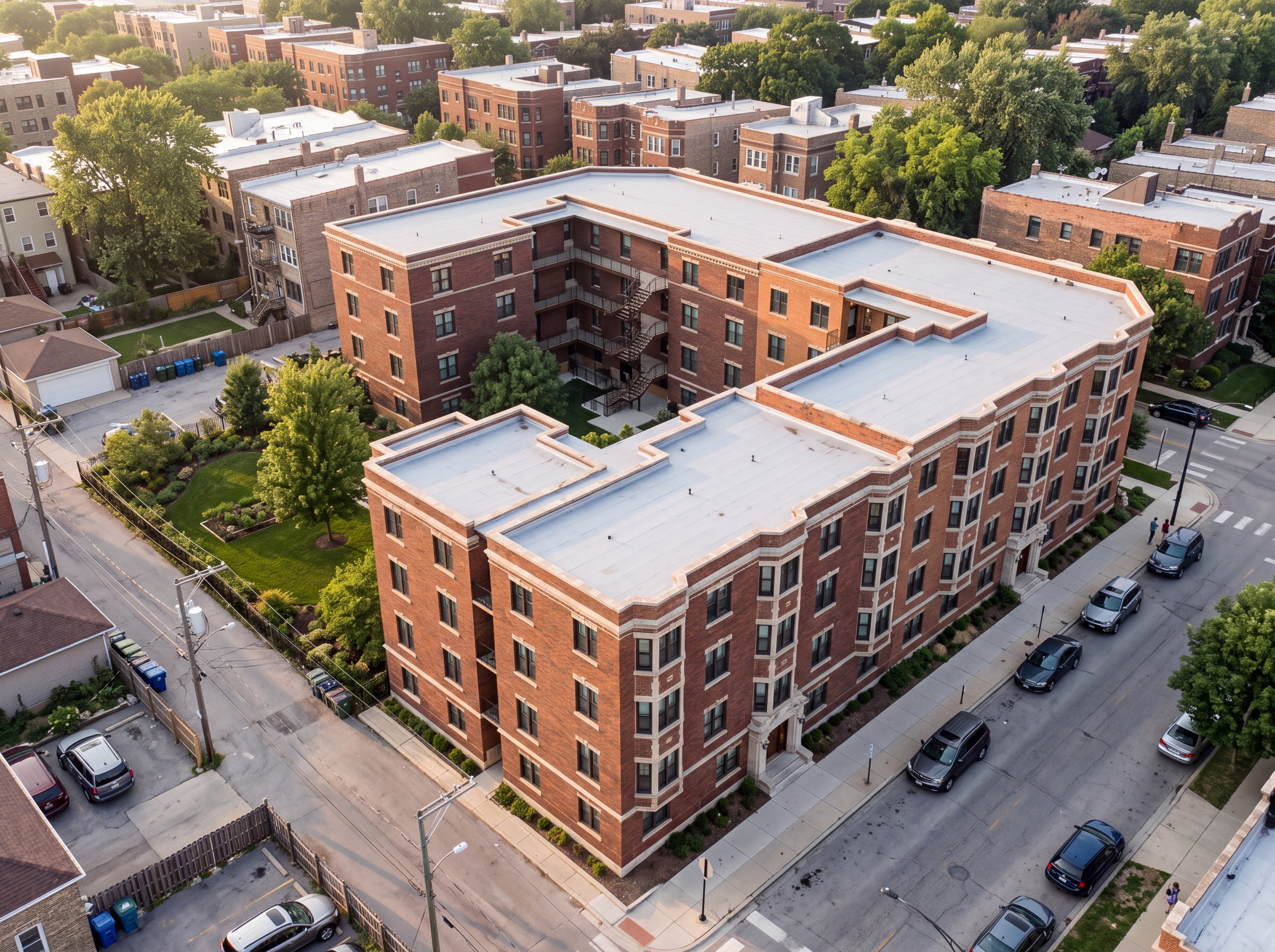 Aerial view of a red-brick courtyard apartment building with landscaped gardens and tree-lined neighborhood streets.
